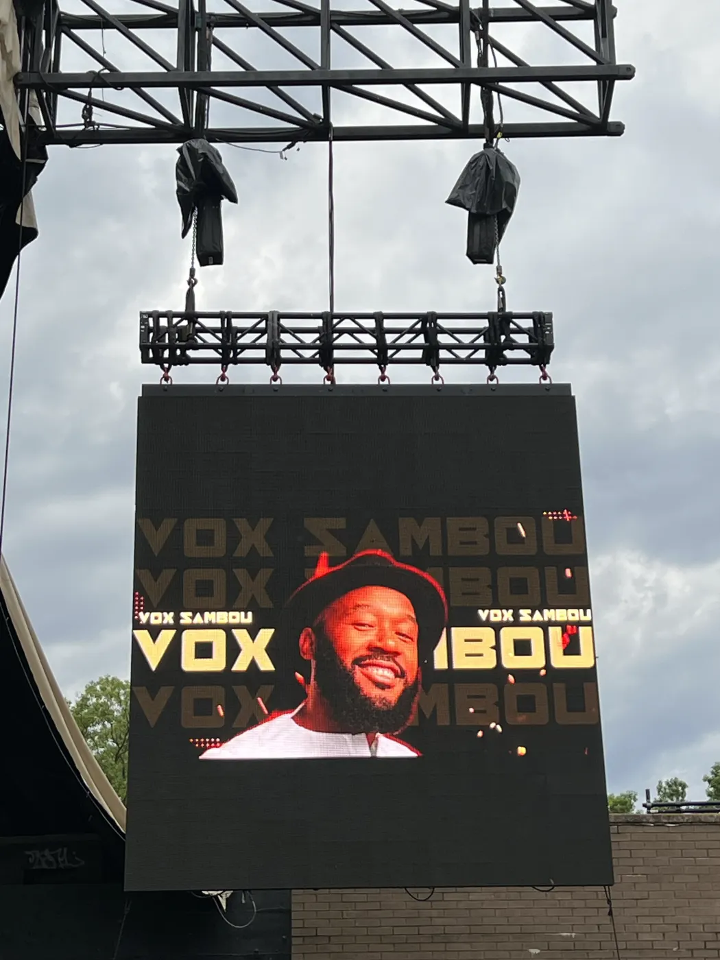 Vox Sambou’s name and face on a giant LED screen hanging from an outdoor stage rig